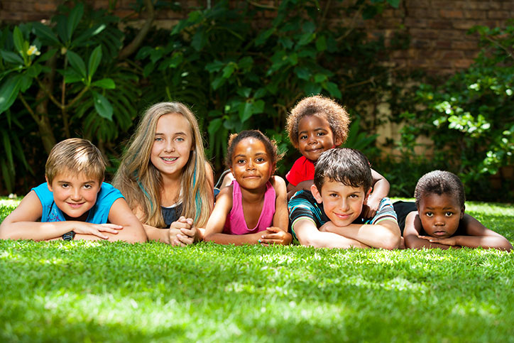 Diverse group of children laying on the grass, facing the camera.