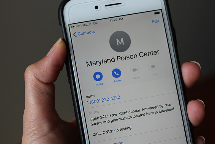 Hand holding a cell phone with the screen on a contact for Maryland Poison Center with the phone number 1-800-222-1222