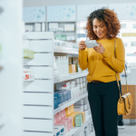 A woman in a drugstore holding a medicine box and reading its label.
