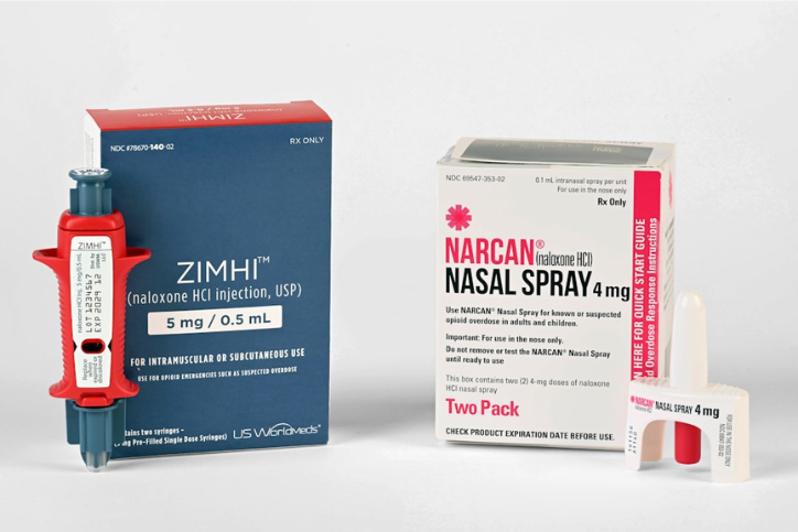 A box of ZIMHI naloxone injection with the device in front of it, next to a box of Narcan naloxone nasal spray with the device beside it.