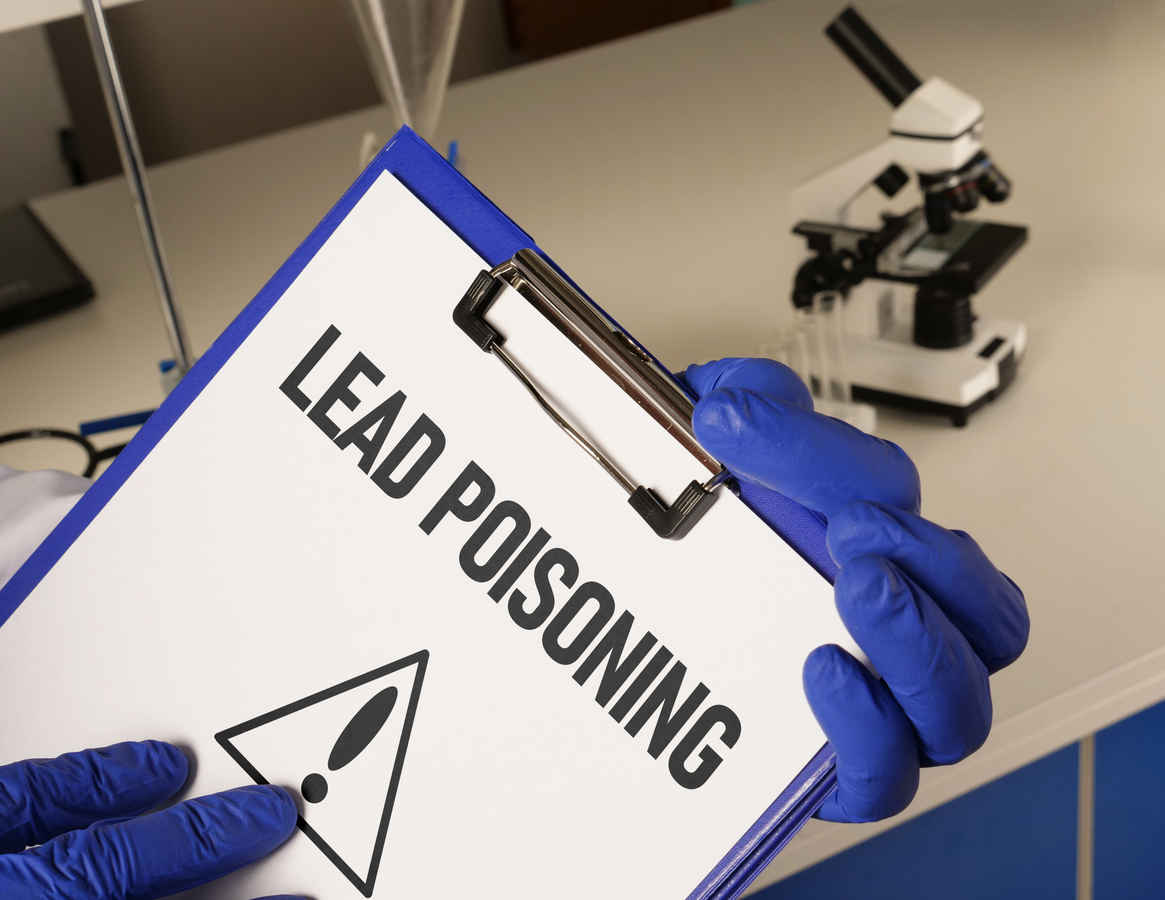 A close-up of a clipboard holding a sheet of paper that says "Lead Poisoning" with a caution symbol.